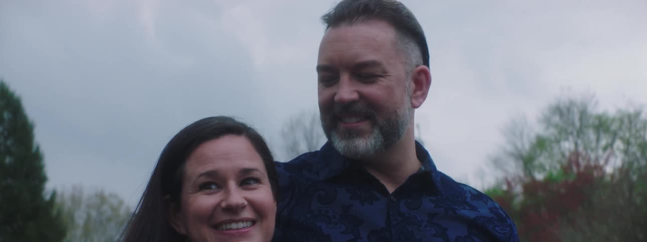 A man has his arm around his wife as they smile and nod and look encouraging