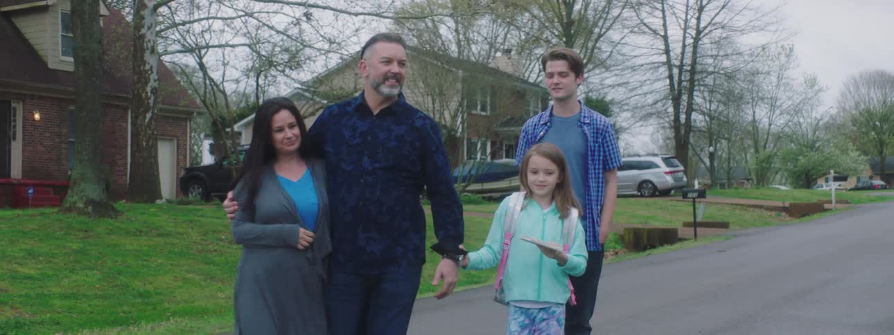 A girl pulls her dad toward a house as the family walks together in a neighborhood