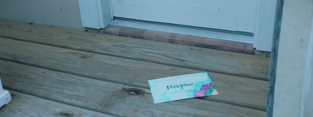 A letter being dropped on the porch in front of the door of a house