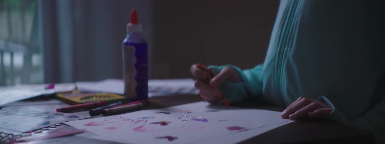 A girl using a crayon to draw on a sheet of paper while sitting at a table