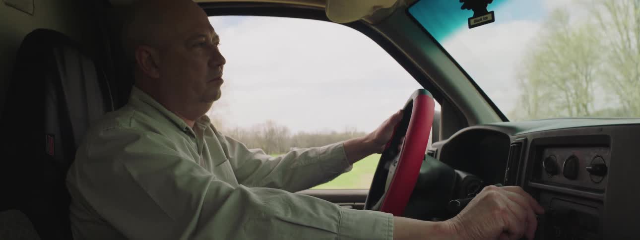 Male reaches for the knob on the radio dial while driving his truck down the road