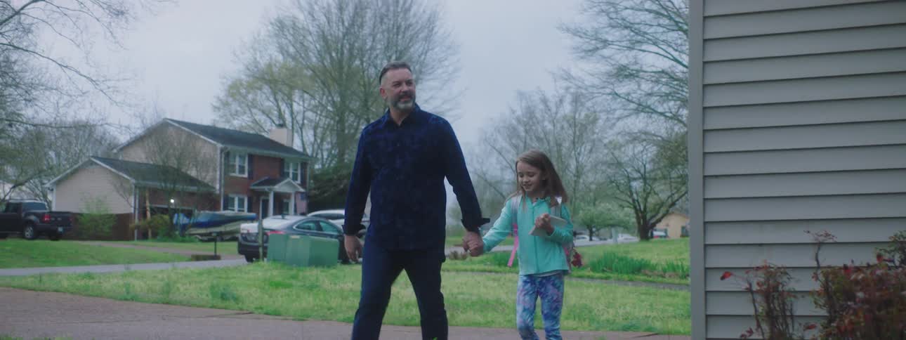 A man and girl holding hands while approach a house to leave a letter on its doorstep