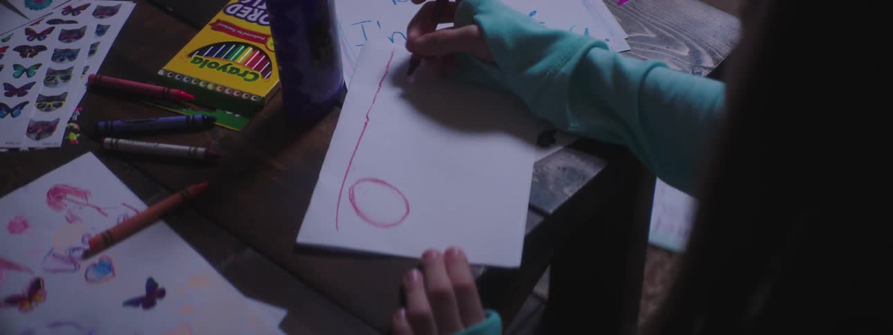 Girl sitting at table draws on paper with crayons