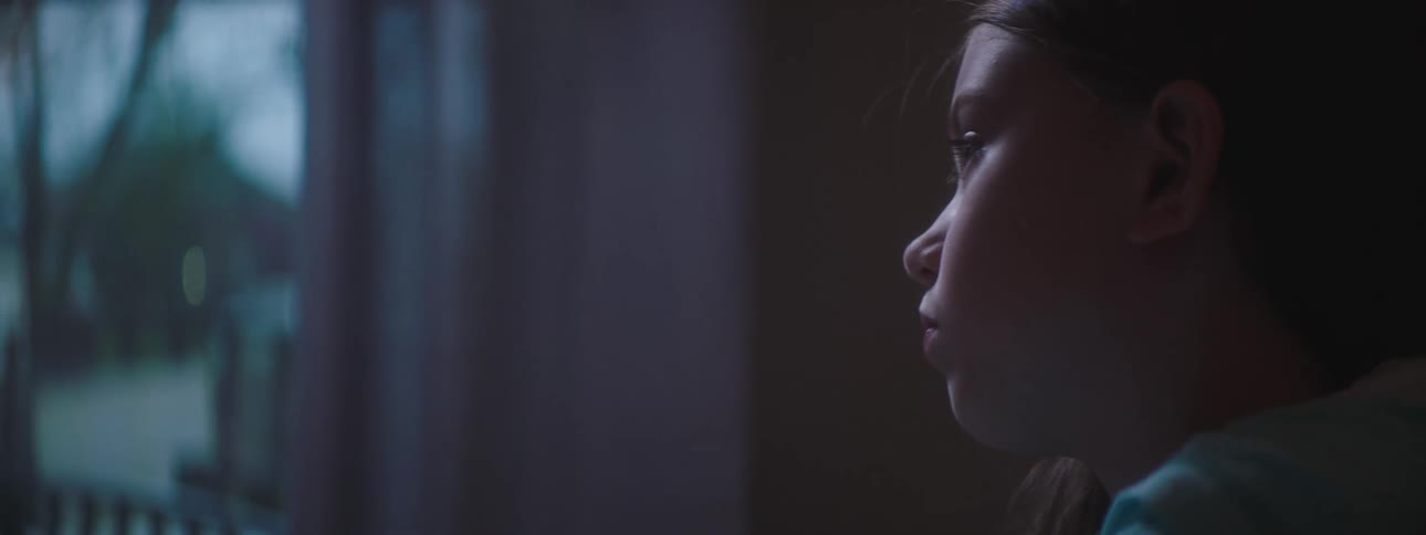 Girl sits looking out room toward street and draws