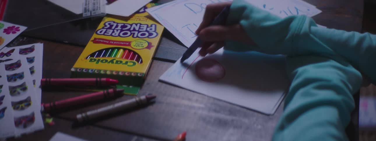 A child uses crayons and pencils to color sheets of paper on a table