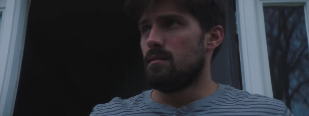 A man picks up a card from his doorsteps looks around confused and walks back inside