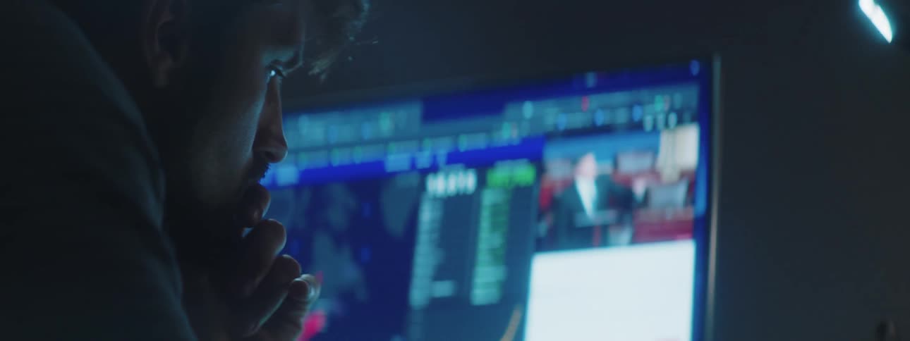 A man sitting in front of a computer at a desk watching a video on the screen