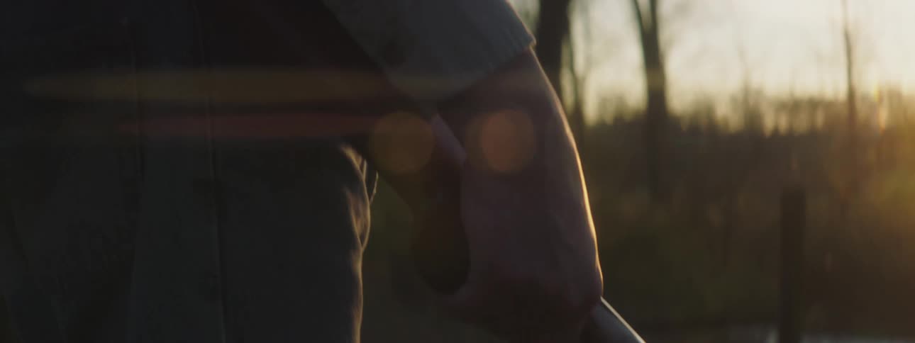 A man standing outdoors talking on a phone with one hand and holding a shotgun with the other