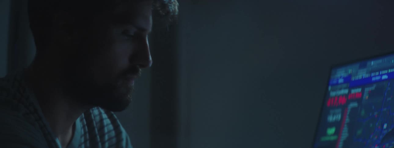 Young bearded man sits in front of computer monitors