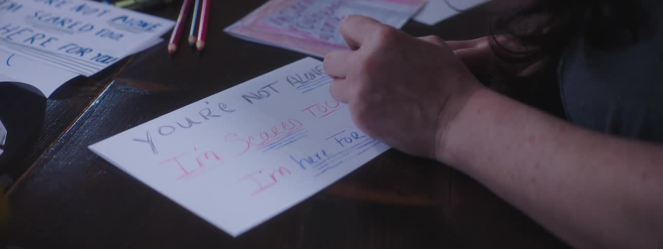 Woman sitting at table writes sign on paper using crayon