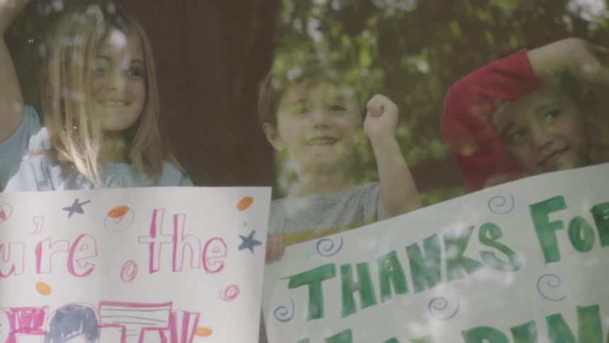 Kids standing in window show welcome signs while waving