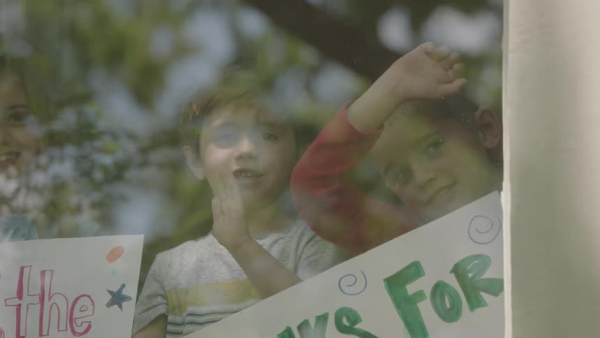 Children are holding thank you signs while smiling and waving from inside a building