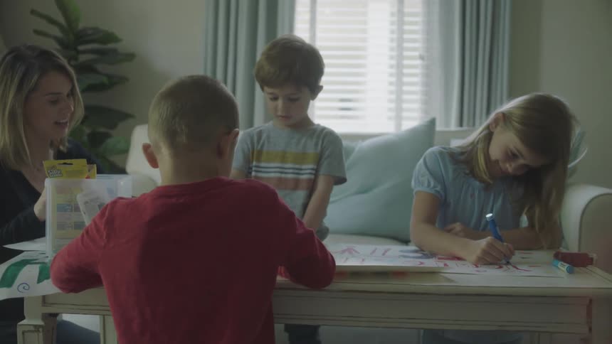 Kids drawing on paper using markers while mother watches smiling