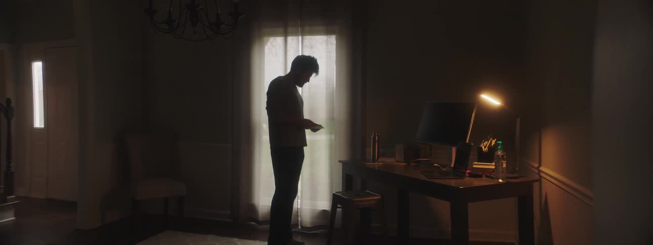 A man walks into a house while going through the mail in hand
