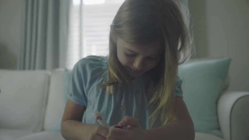 A girl using a marker to draw while sitting in the living room of a house