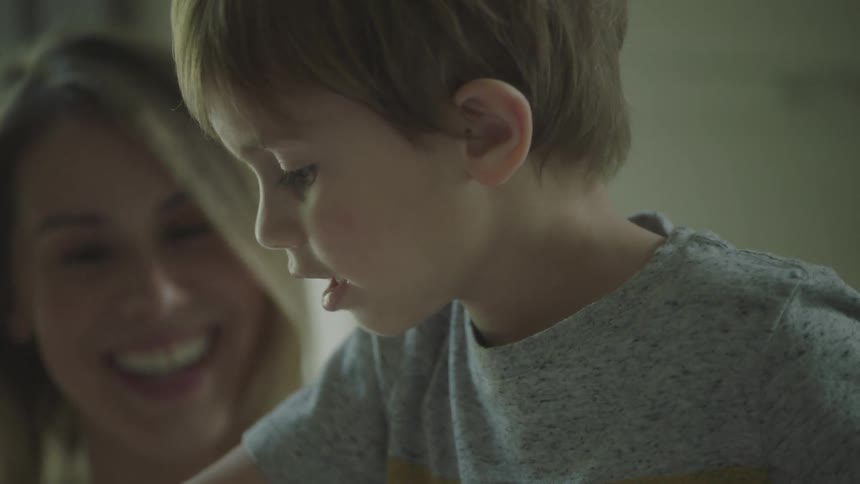 Kid picks up markers from box while mother watches smiling