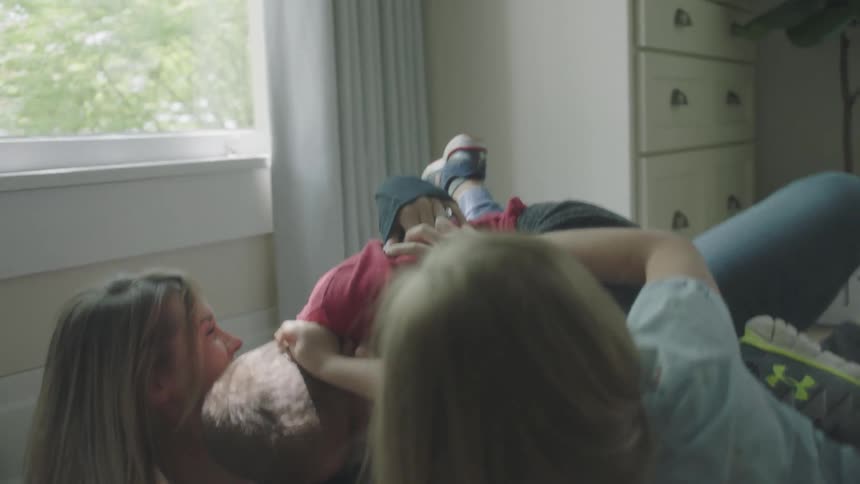 A mom lies on the floor with her three children piled on top tickling and laughing and playing with them