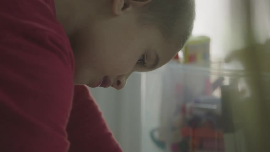 Girl concentrates down on table as another person sets plastic tub on table
