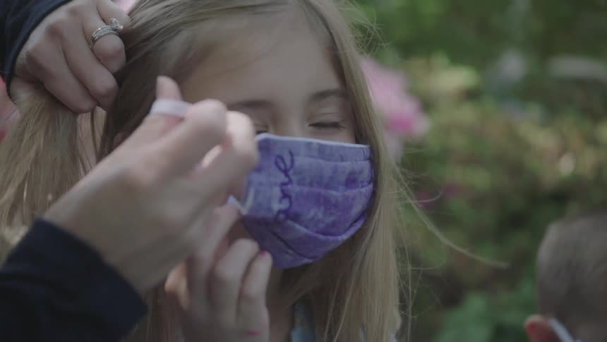 An adult helping a girl to put on a purple face mask