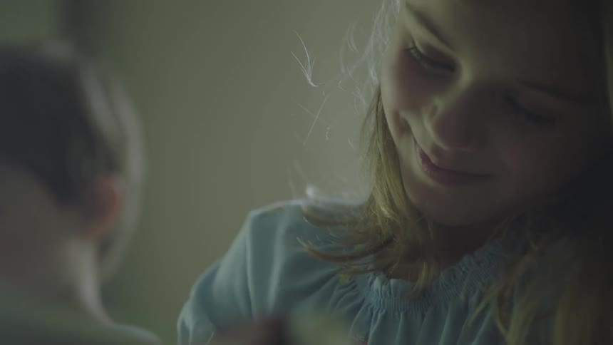 A girl with her head tilted smiles as she draws