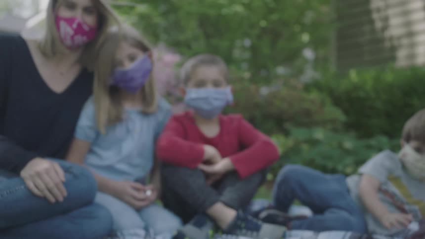 Mother and kids wearing face masks sit on the grass in the garden