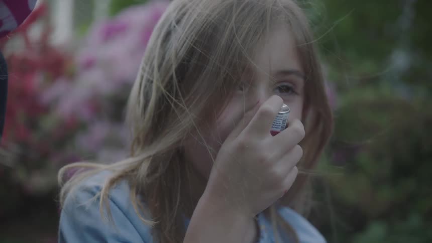 Girl sitting outdoors uses inhaler