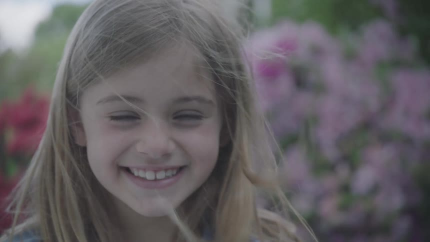 Little blonde girl smiles broadly in the garden