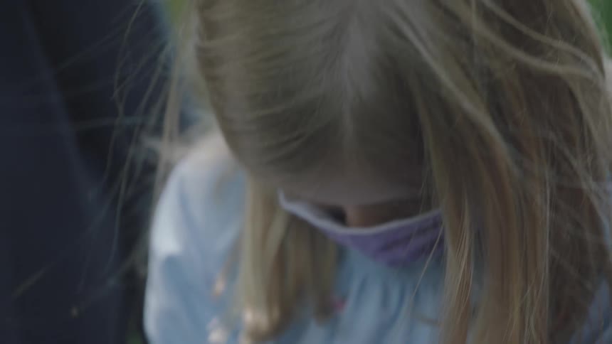Girl sits outdoors with others removing face mask to use inhaler