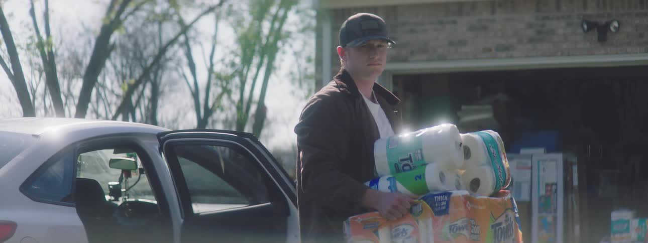 A man carries paper products from his car to his garage