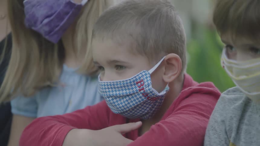 A young family in face masks stand outside next to each other