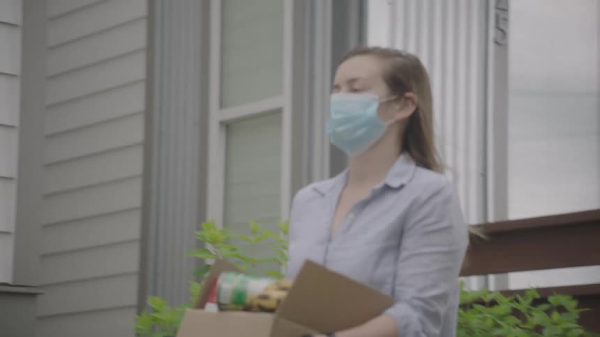 Woman walks and carries a cardboard box full of food as a precaution during the lockdown