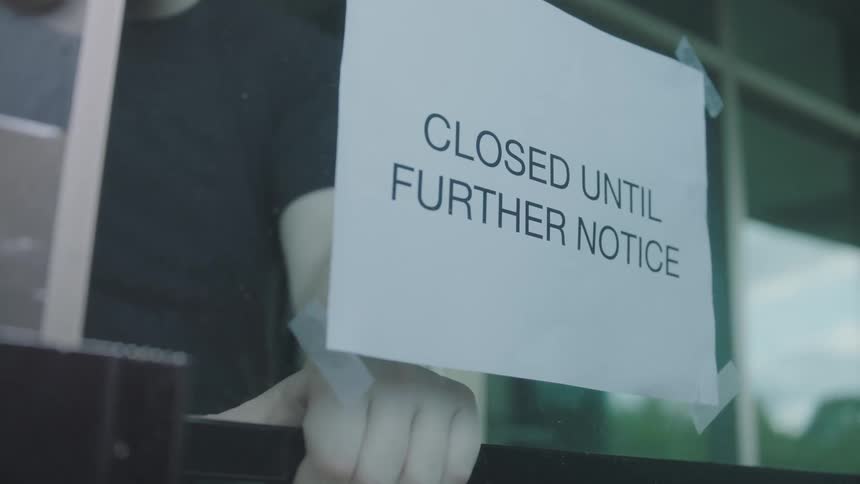 A person hangs a closed sign on the door of a shop