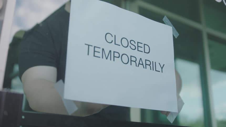 Man closes store door and places a closed sign on the glass