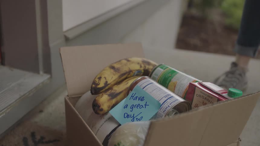 Woman wearing gloves delivers groceries in cardboard box