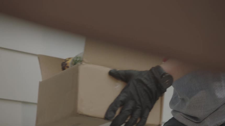 Woman wearing mask and gloves delivers box with groceries at home doorstep