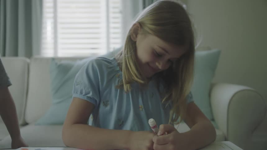 A girl kneeling at the coffee table smiling and using markers to color in a large poster