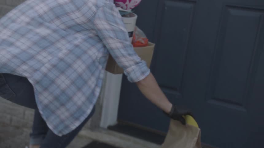Woman wearing face mask and gloves delivers groceries at doorstep