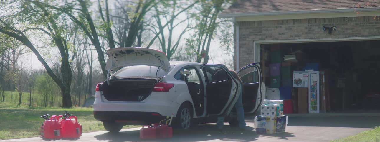 Man unloads groceries from open car parked in driveway near open garage