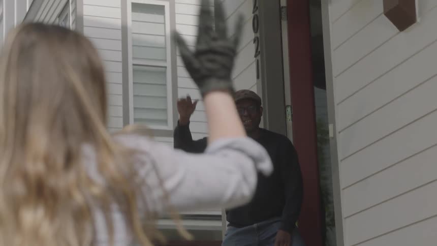 A young woman drops off a delivery of items for a man and he steps out of his home to pick them up