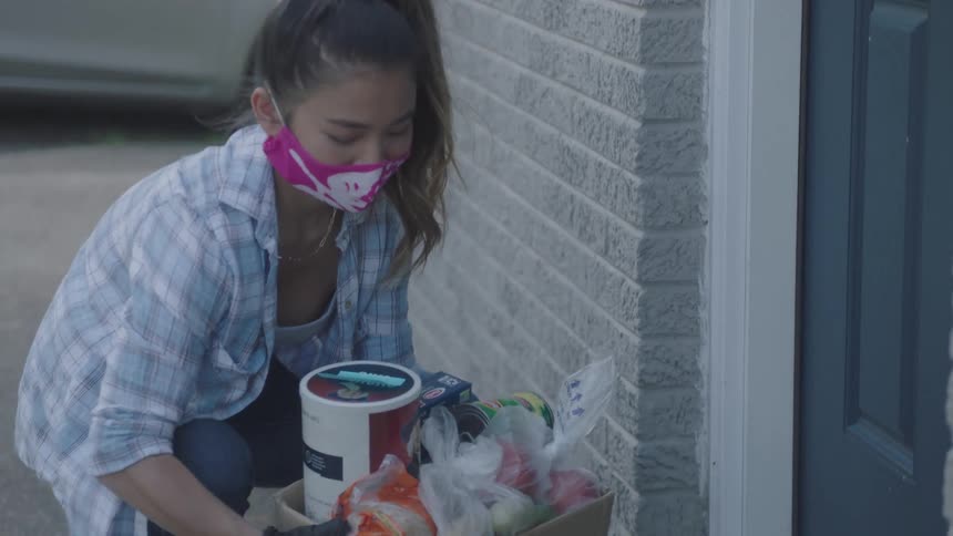 A teenage woman placing a box of food in front of the door of a house before knocking on the door