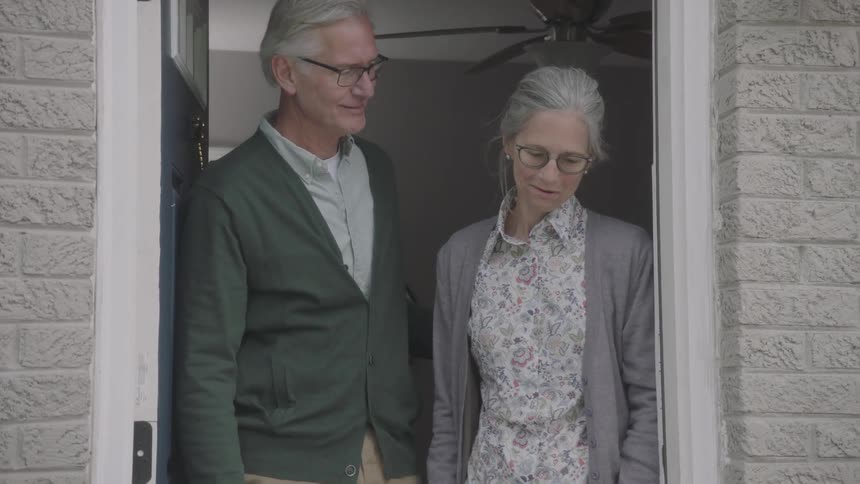 Older couple open door to wave then pick up delivered groceries