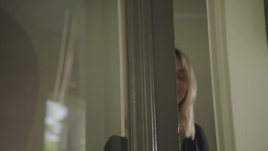 A woman smiles as she looks outside and opens the door and heads out