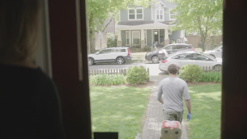 Male wearing a face mask delivering supplies to a woman at her front porch during pandemic