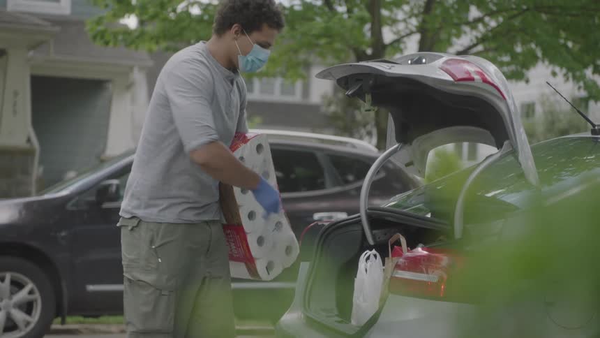 A man taking a large package of tissue and a plastic bag from the trunk of a car and carrying it away