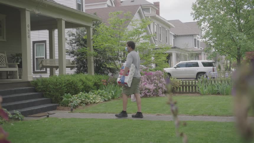 Man wearing face holding groceries walks to house