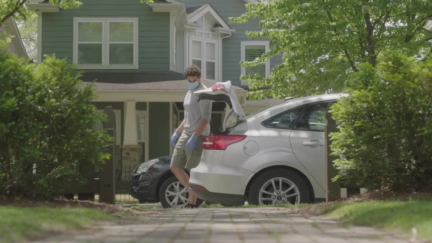 Man wearing a face mask opens the car trunk and takes toilet paper and food bag