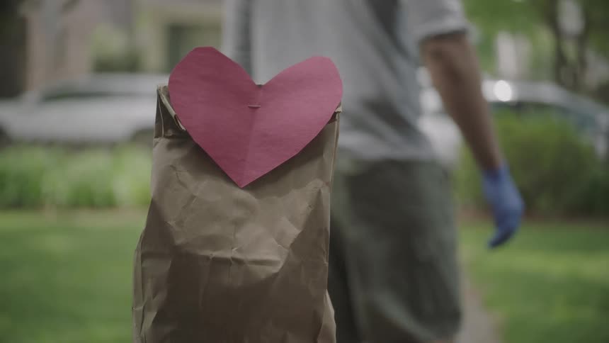 Man places paper bag with attached red paper heart on porch of house