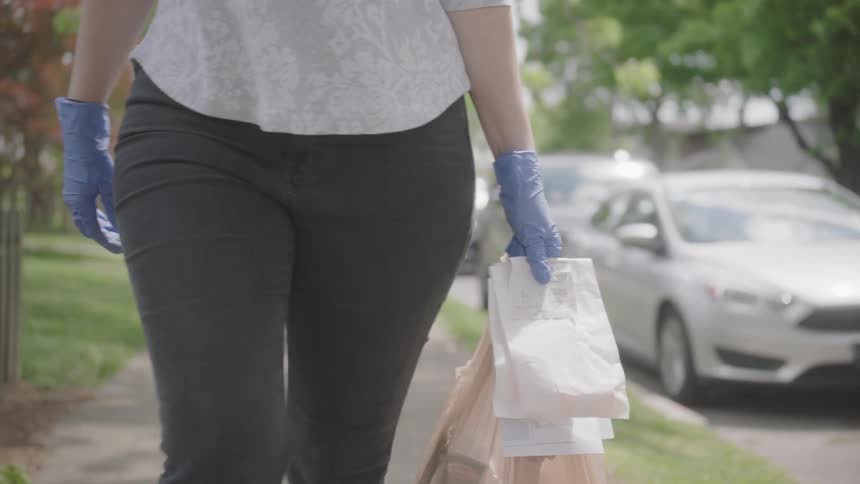 A woman walks on a sidewalk carrying bags
