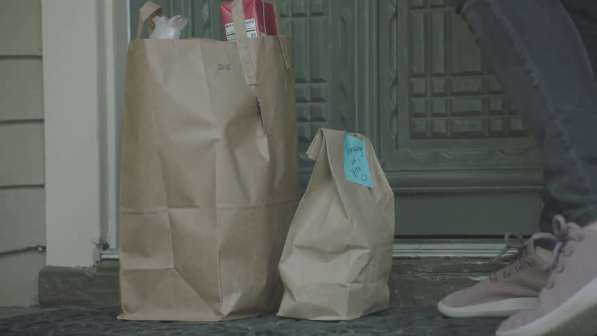 A person delivers groceries to a house and knocks on the door