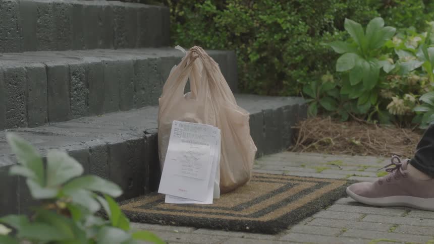 A woman leaving a plastic bag and note on at rug at the base of a staircase